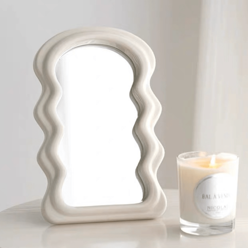 A cream-colored ceramic table squiggly mirror with a wavy sculpted frame perfect for decorative use