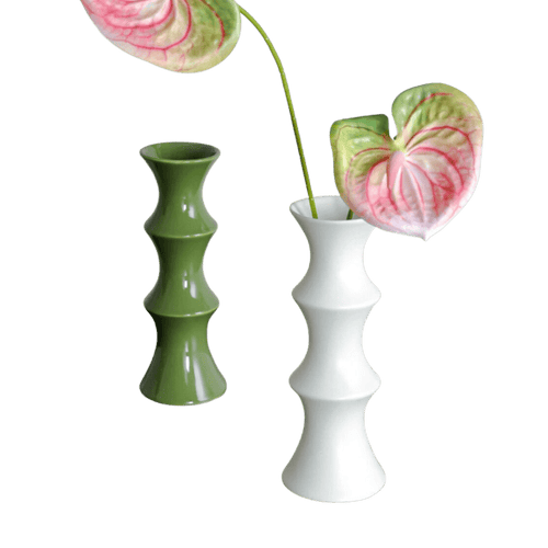 Two ceramic bamboo vases in matte olive green and glossy white each holding a heart-shaped anthurium flower