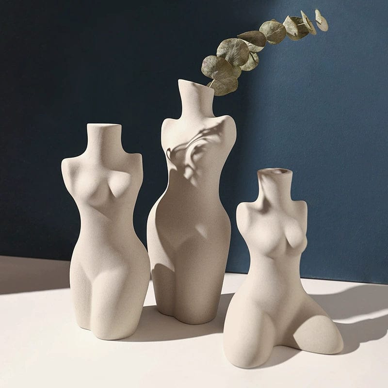 Three minimalist body shaped vases in white ceramic with varying poses one holding a eucalyptus branch