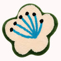 Cream-colored plush magnolia flower shaped rug with green border and blue center with black dot accents