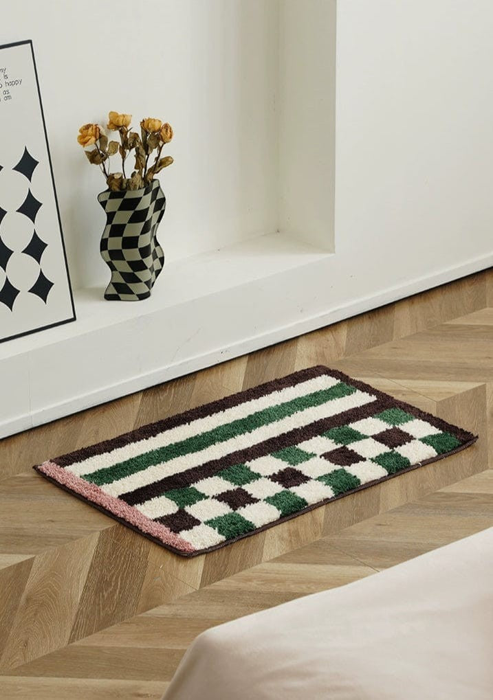 Rectangular plush bath mat with green and white checkered pattern bordered by dark brown stripes and pink edge