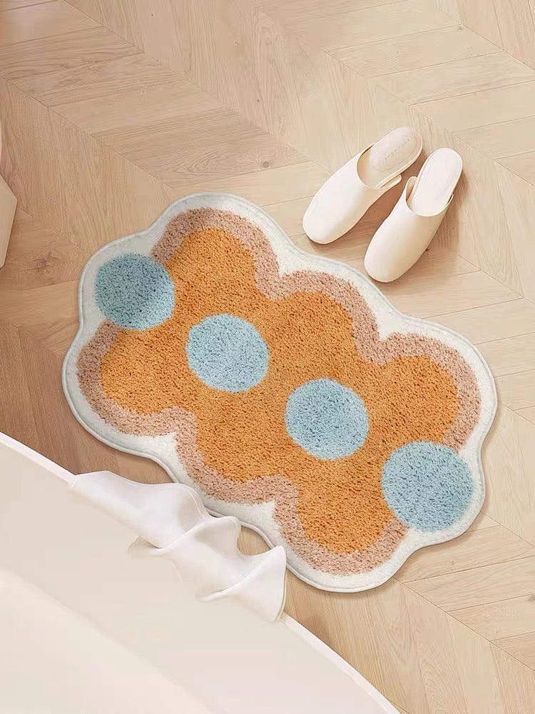 A plush orange cloud shaped bath mat with light blue circular accents and a white border for bathroom use