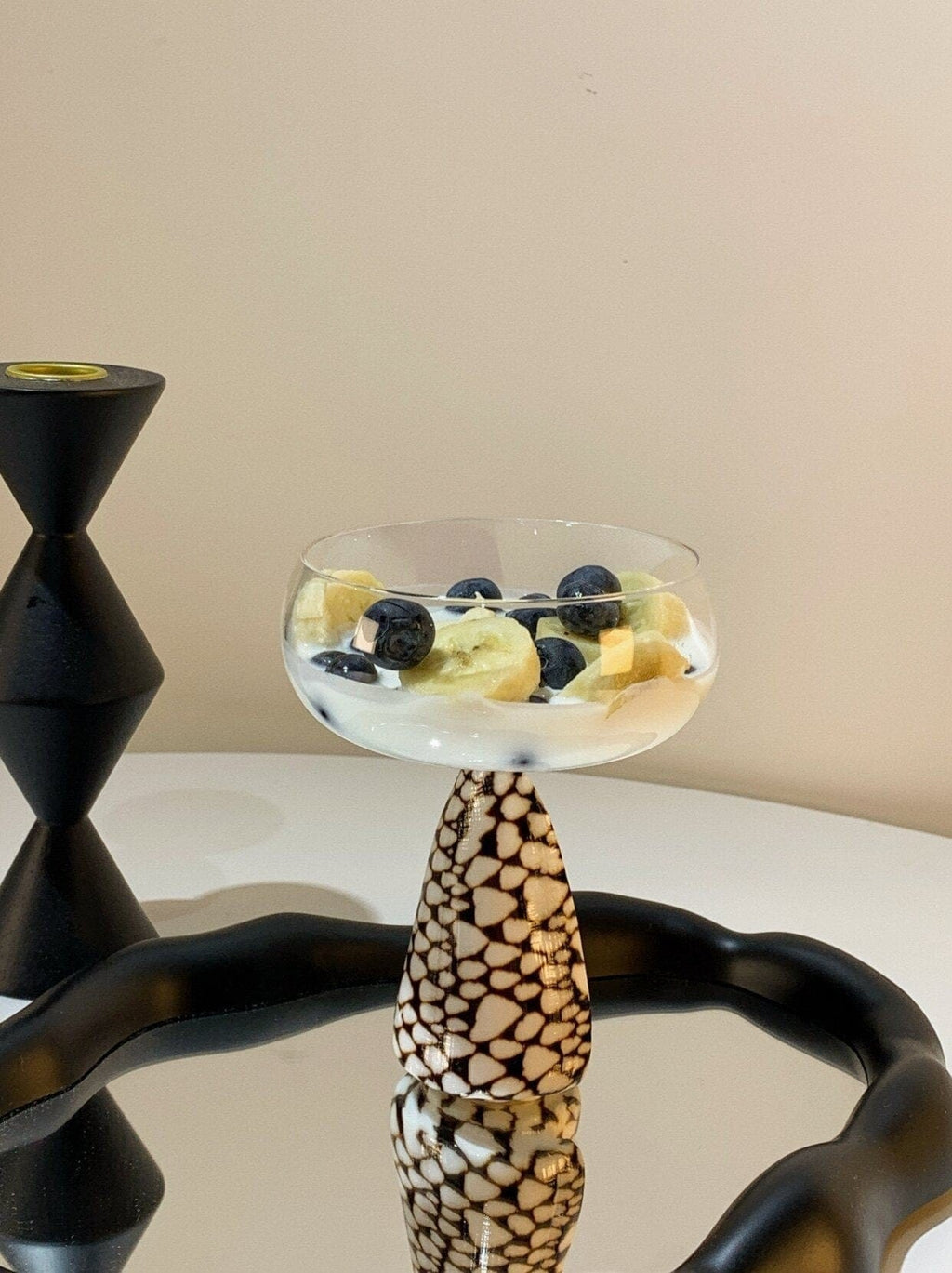 Clear glass conch shell coupe glass dessert bowl filled with yogurt and sliced fruit on black patterned pedestal