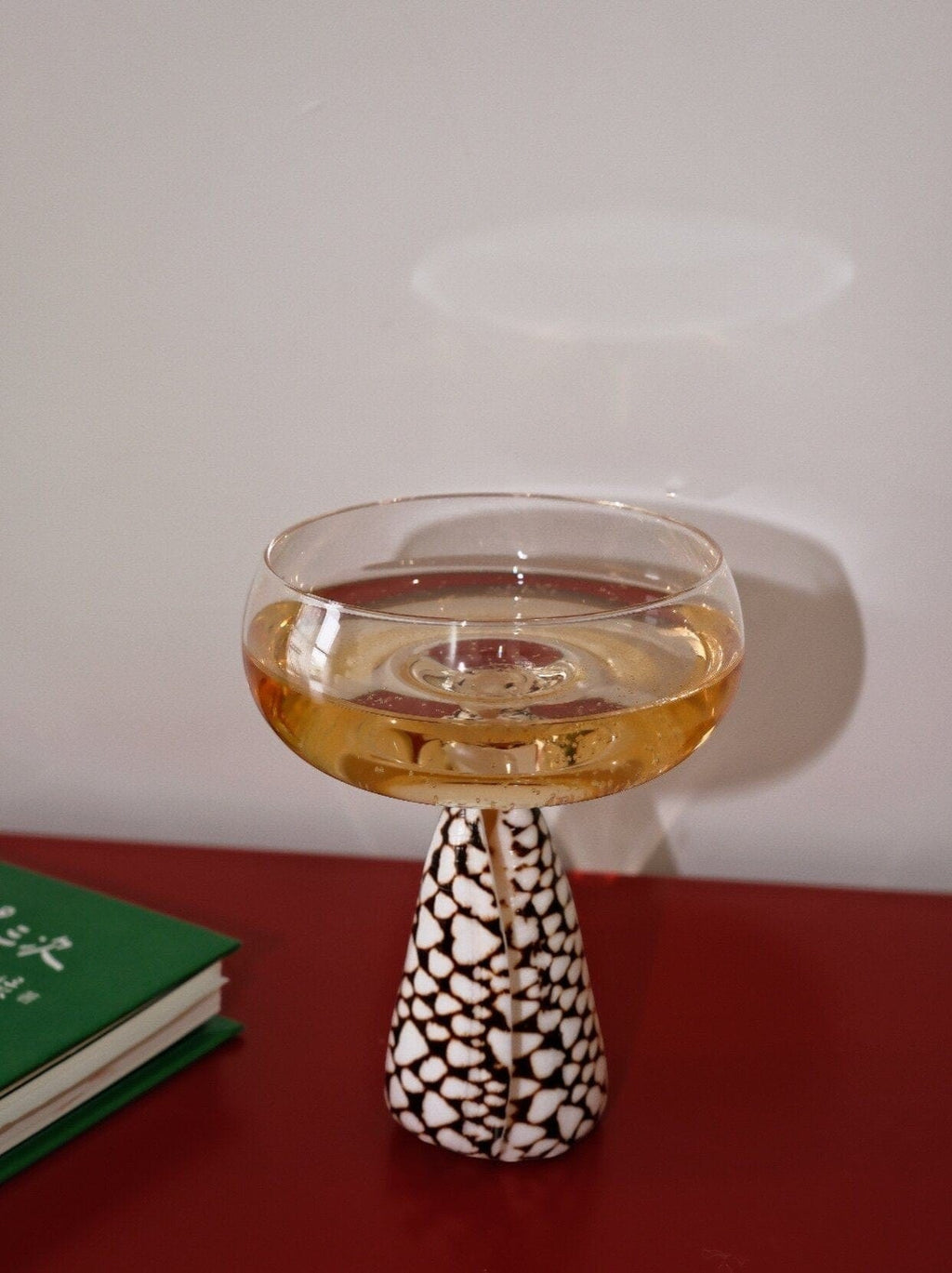 A clear glass conch shell coupe glass with a wide bowl and slender stem filled with golden liquid