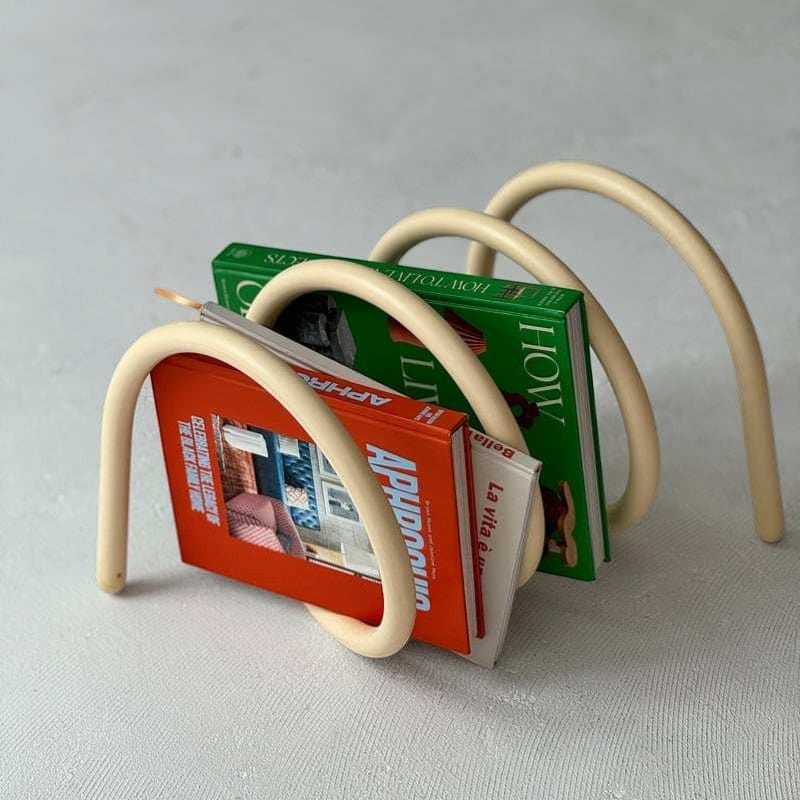Cream-colored curved metal spring book holder with minimalist design for organizing books on shelves
