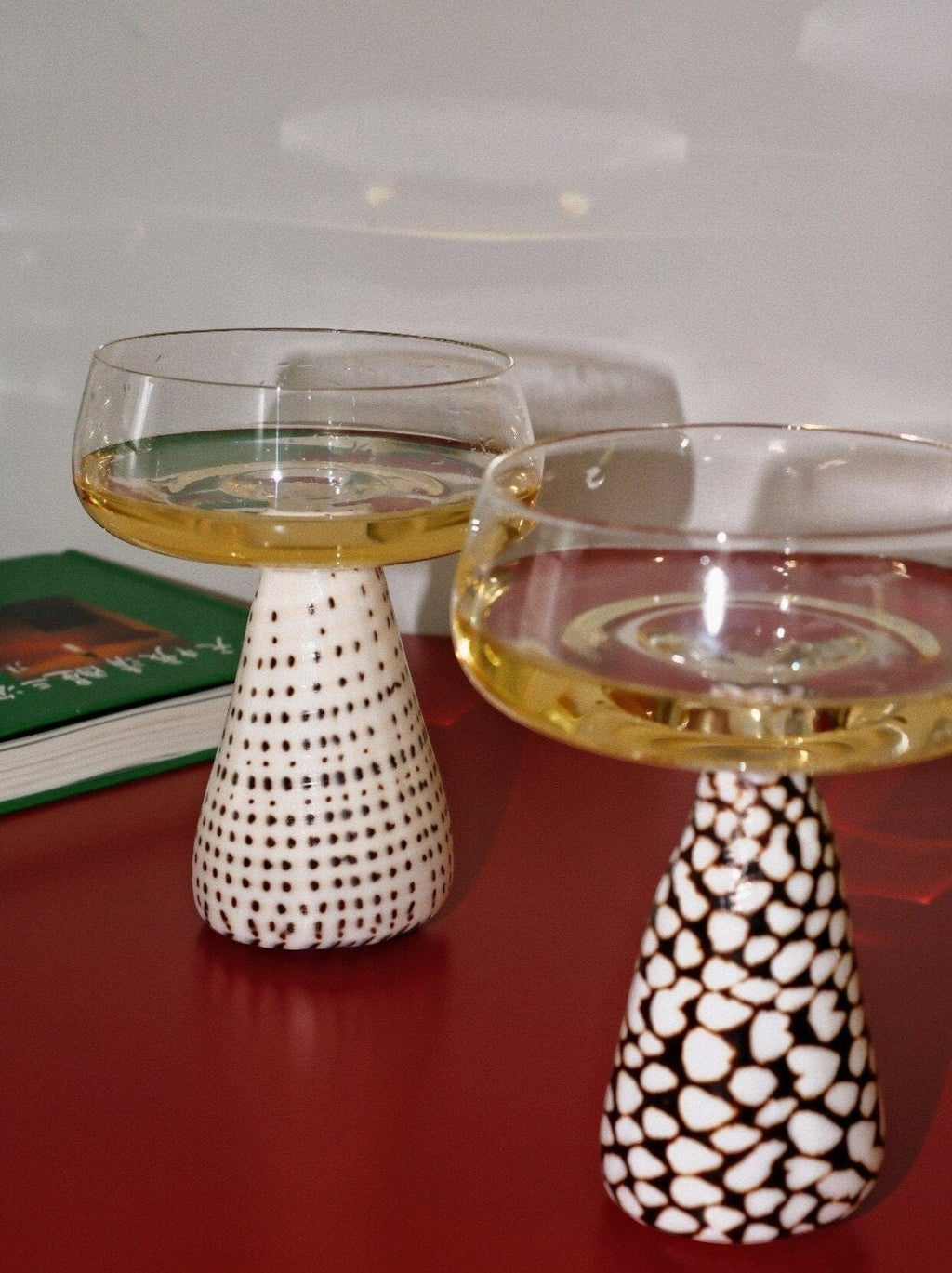 Two elegant white ceramic conch shell coupe glasses with black polka dot and stone-like patterned bases filled with golden liquid