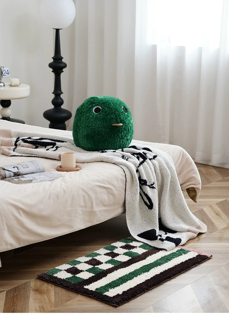 Green plush frog-shaped pillow with black button eyes and tan stitched mouth on retro checkered plaid rug green dark brown