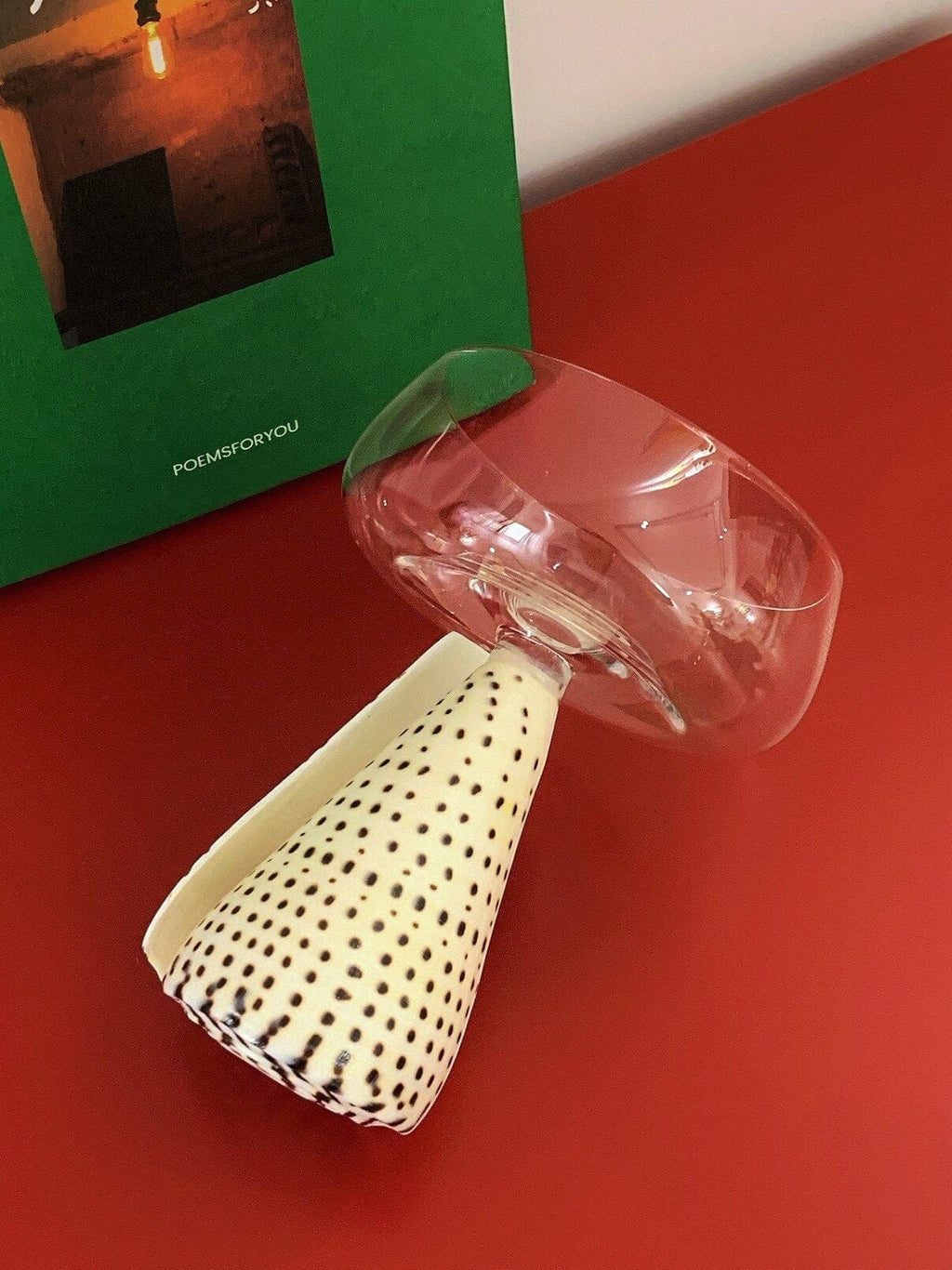 A clear faceted glass tumbler with wide rim on an off-white conical base with black polka dots conch shell coupe glass