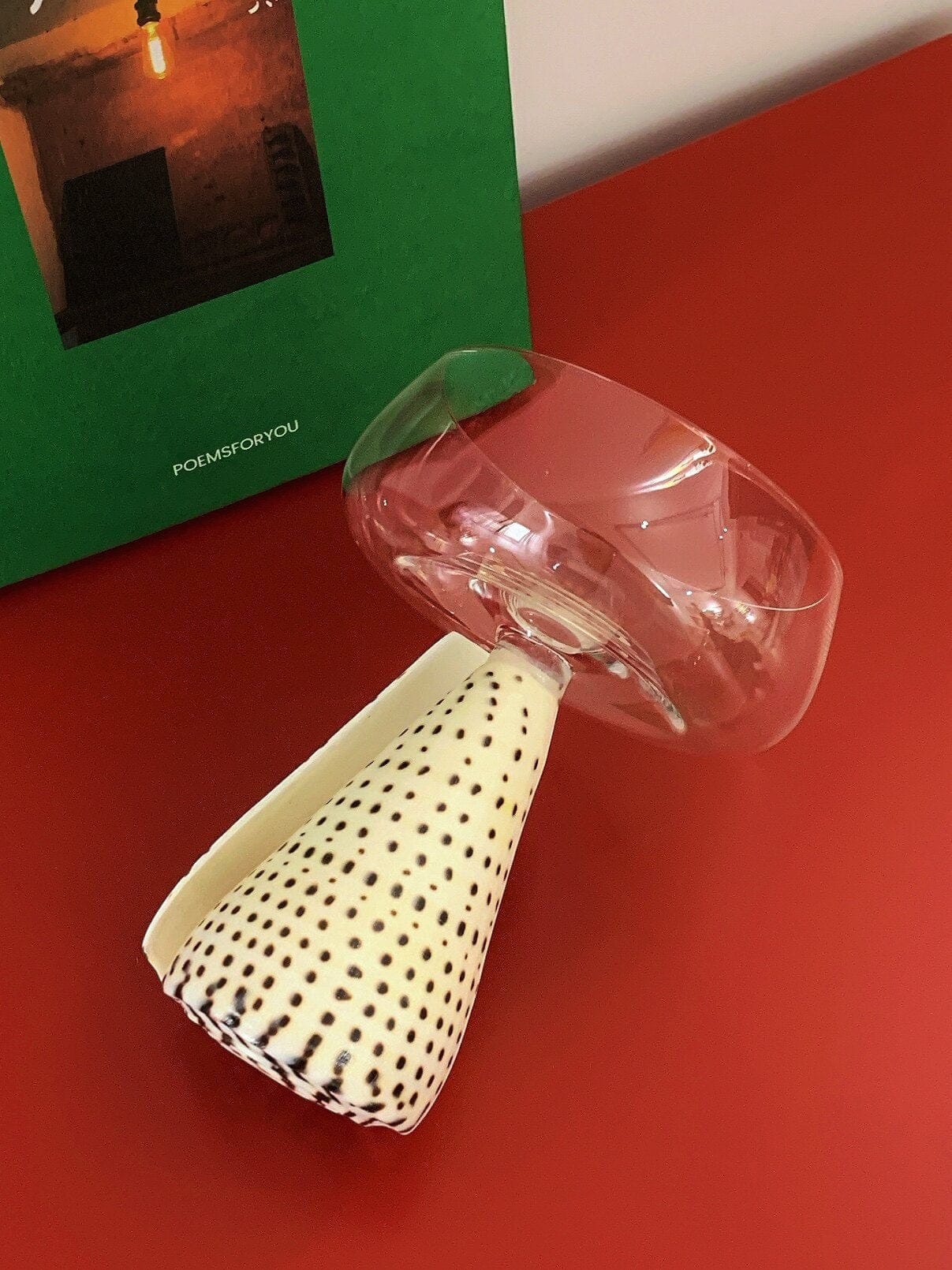 A clear faceted glass tumbler with wide rim on an off-white conical base with black polka dots conch shell coupe glass