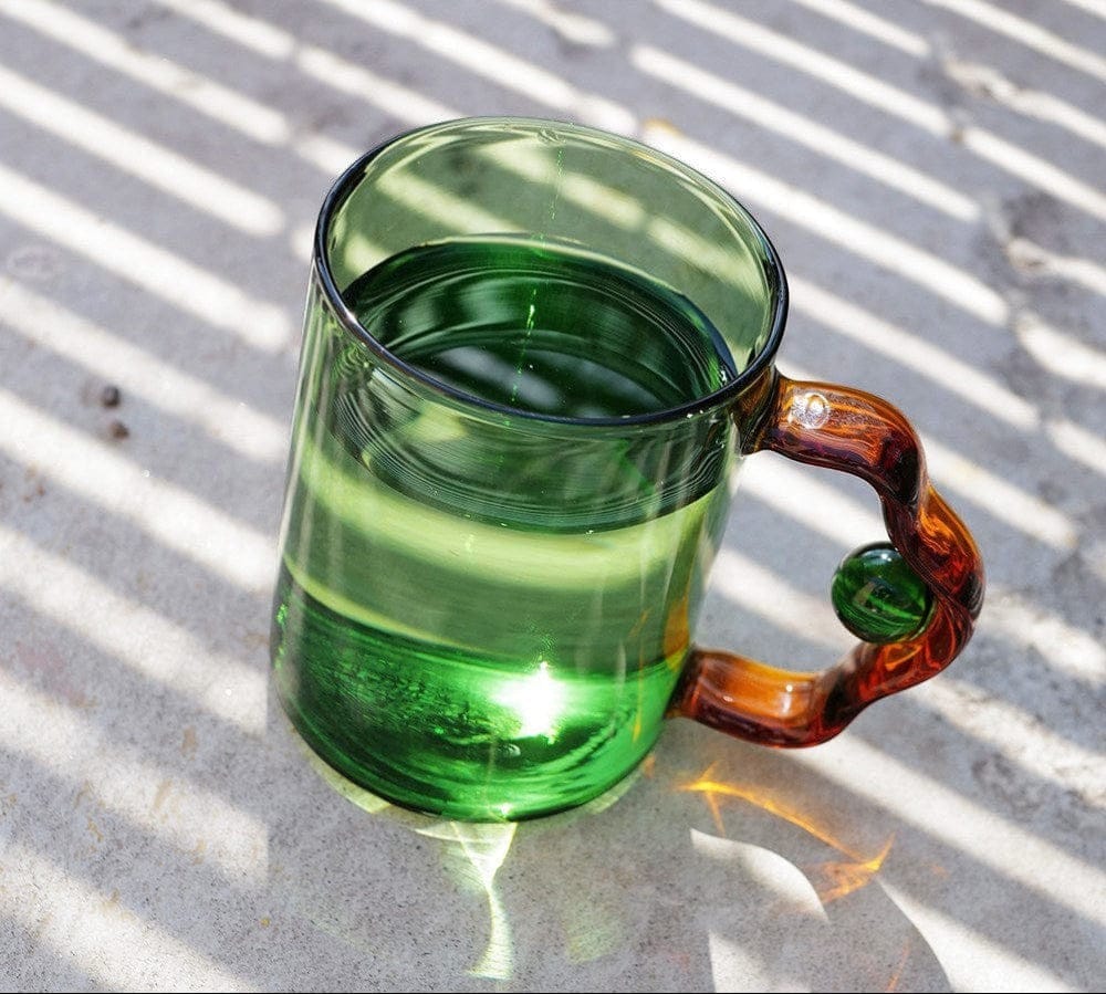 A translucent green glass color block bead mug with a twisted amber handle and a small green bead accent