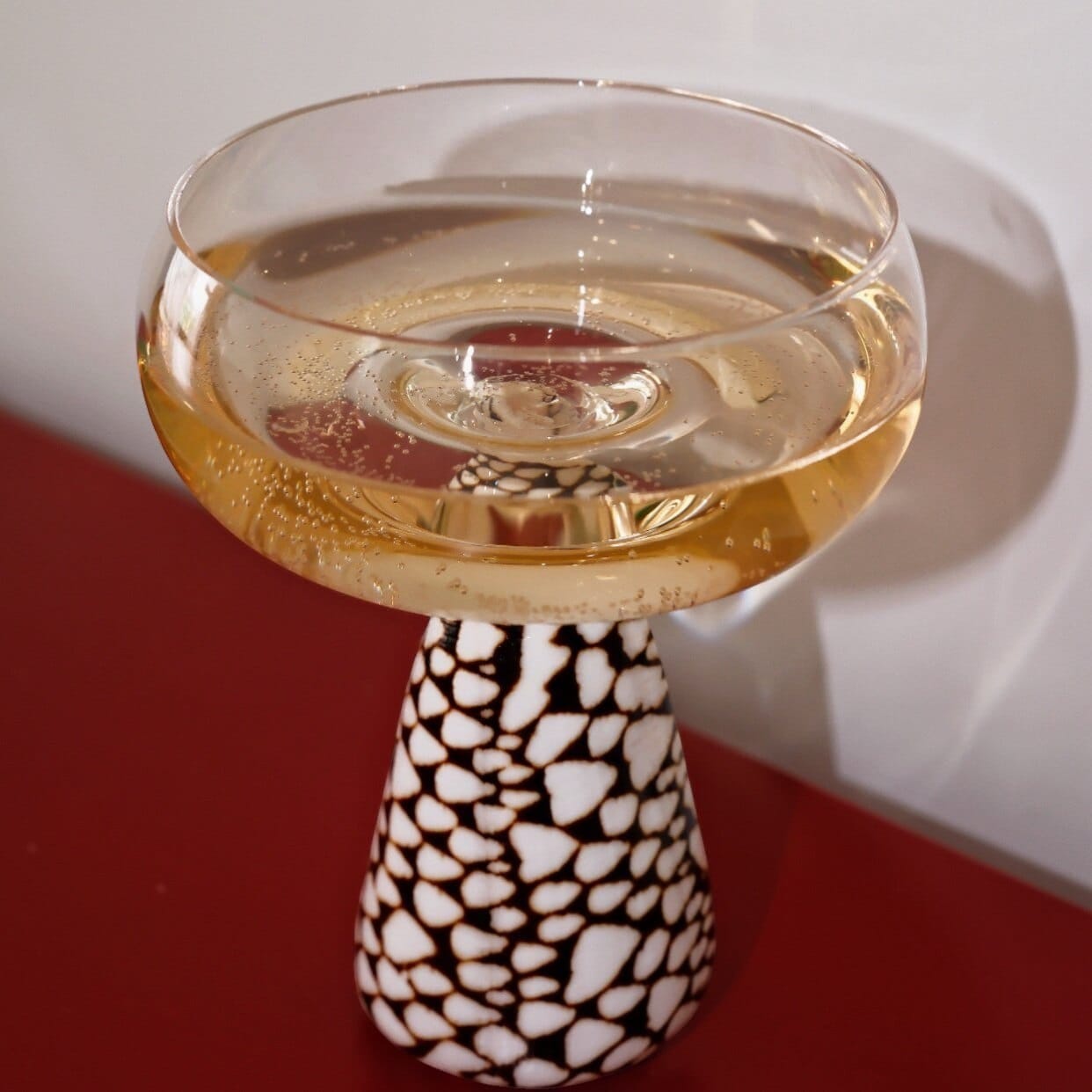 A clear glass conch shell coupe glass filled with golden bubbly liquid resting on a mosaic pedestal base