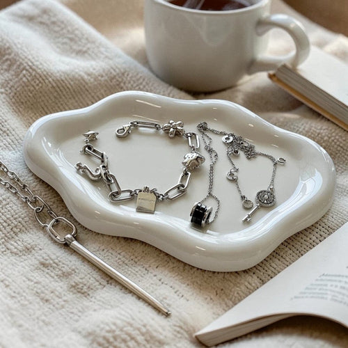 A white ceramic cloud tray with a smooth glossy finish holding silver-toned jewelry pieces