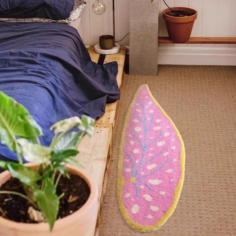 Pink leaf-shaped rug on a carpeted floor next to a bed and plant