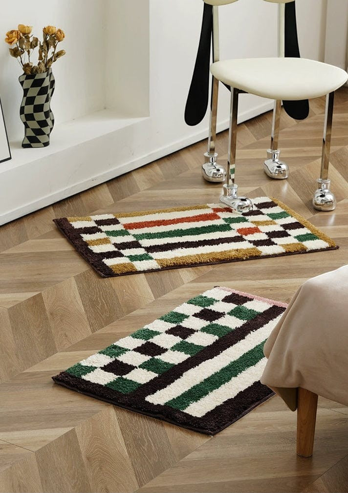 Two rectangular plush bath mats with a retro checkered plaid pattern in green and dark brown on wooden floor