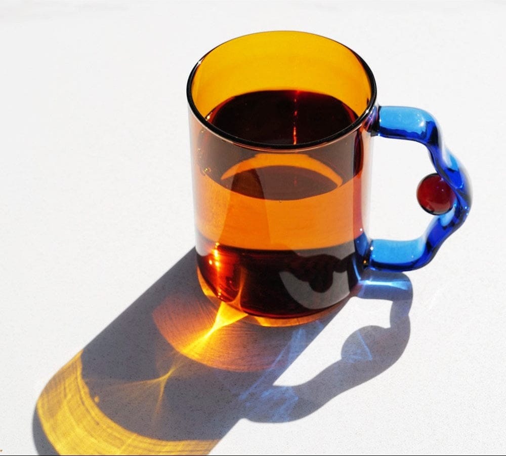 A vibrant amber glass color block bead mug with a sculpted blue handle red bead accent filled with dark liquid