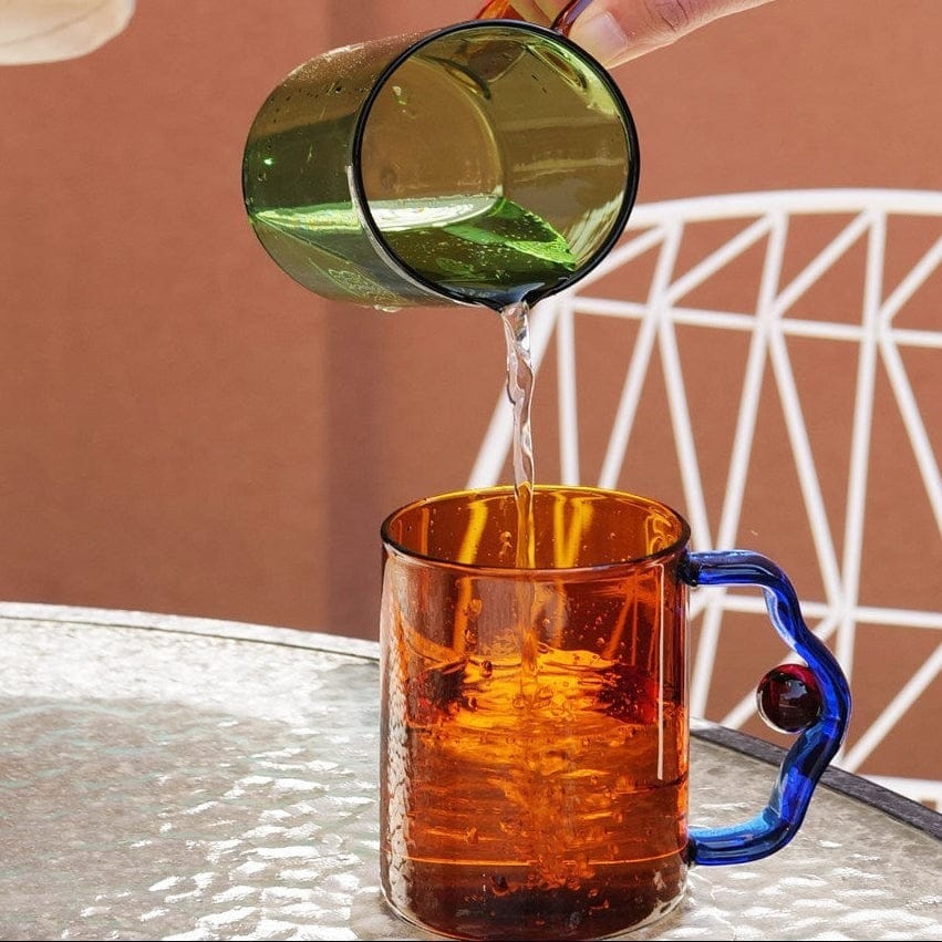 A vibrant amber glass color block bead mug with a sculpted blue handle and a glossy textured surface