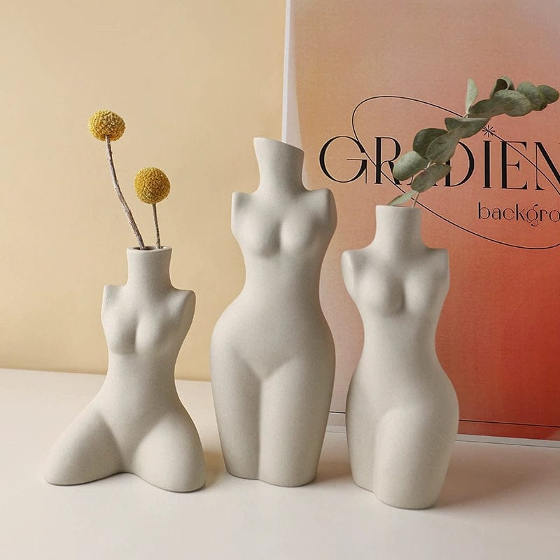 Three white ceramic body shaped vases with stylized female figures holding dried flowers in distinct poses