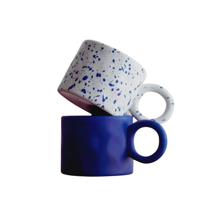 White ceramic dumbo mug with blue speckles stacked on a solid cobalt blue ceramic mug for everyday use