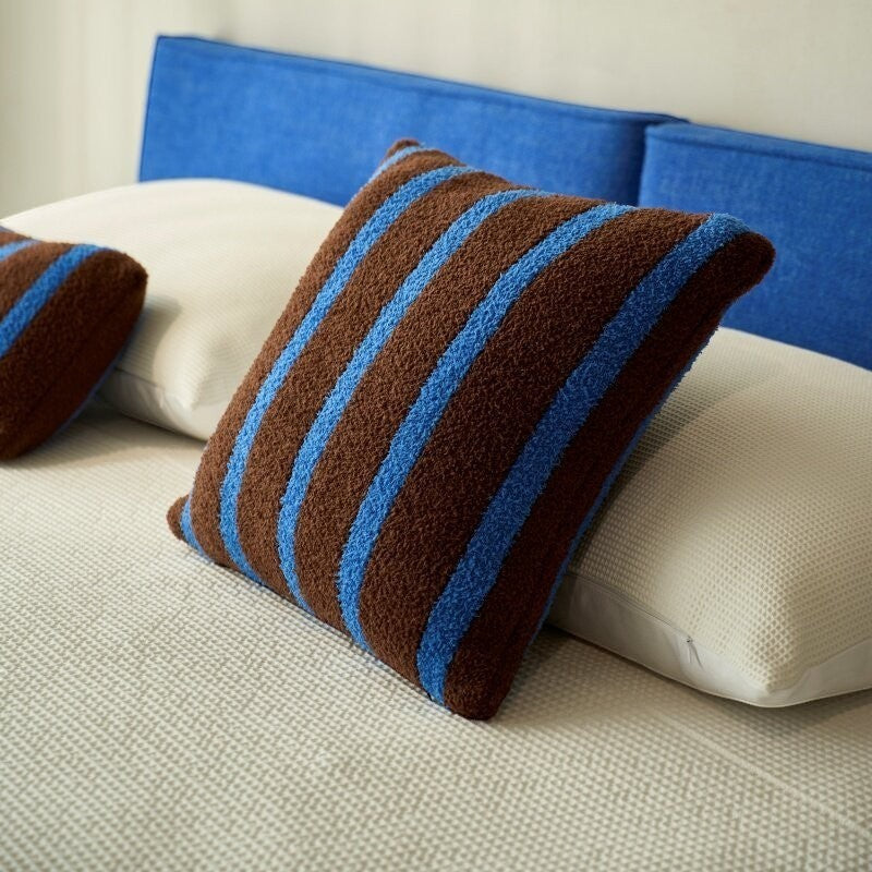 Brown and cobalt blue striped boucle throw pillow on a bed with blue headboard