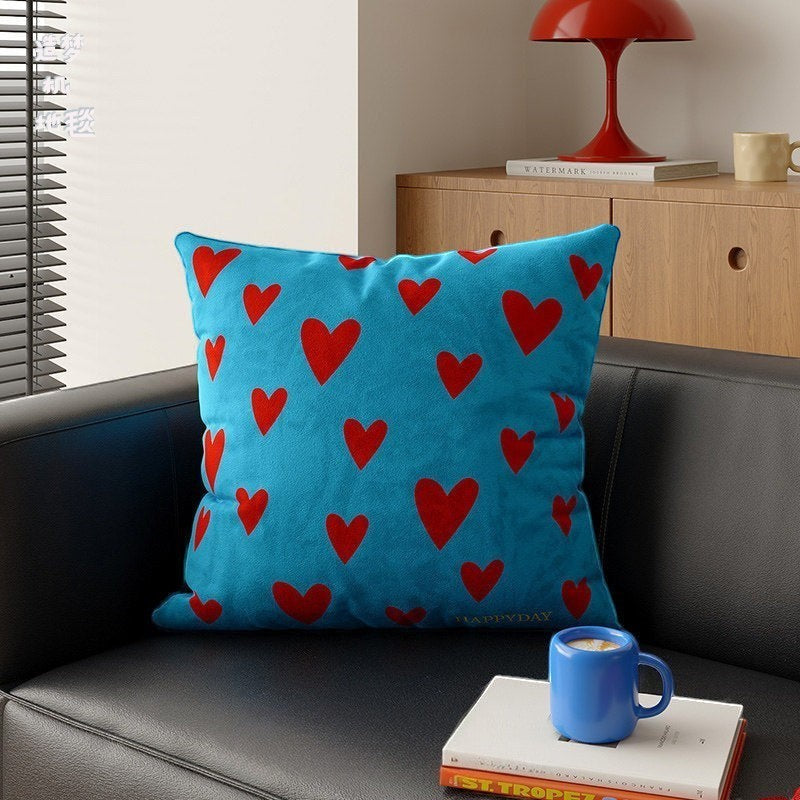 HOMELIVY blue throw pillow with red heart pattern on a black sofa in a cozy living room setting.