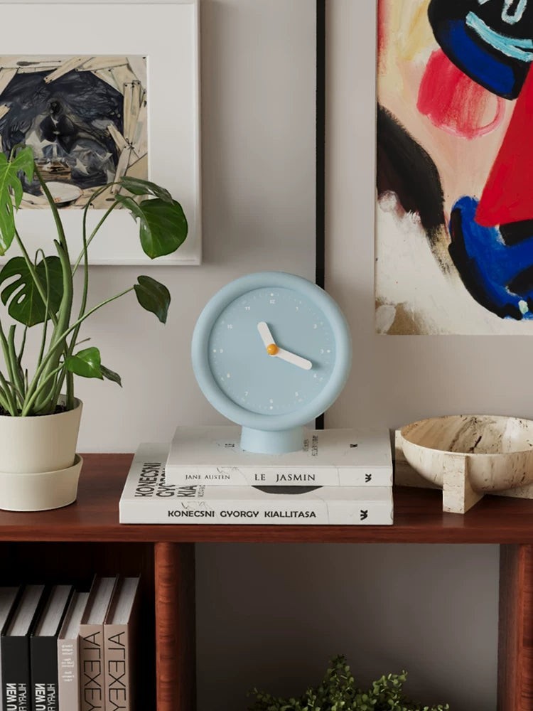 HOMELIVY powder blue minimalist desk clock with white hands and a pedestal base, set on books.