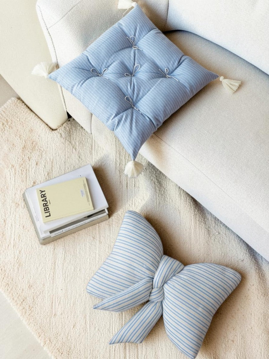 HOMELIVY blue and white striped bow-shaped cushion on a textured rug next to a tufted square seat pad on a sofa.