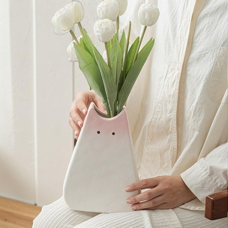minimalist white ceramic cat vase with a soft pink gradient, held by a person with white flowers.