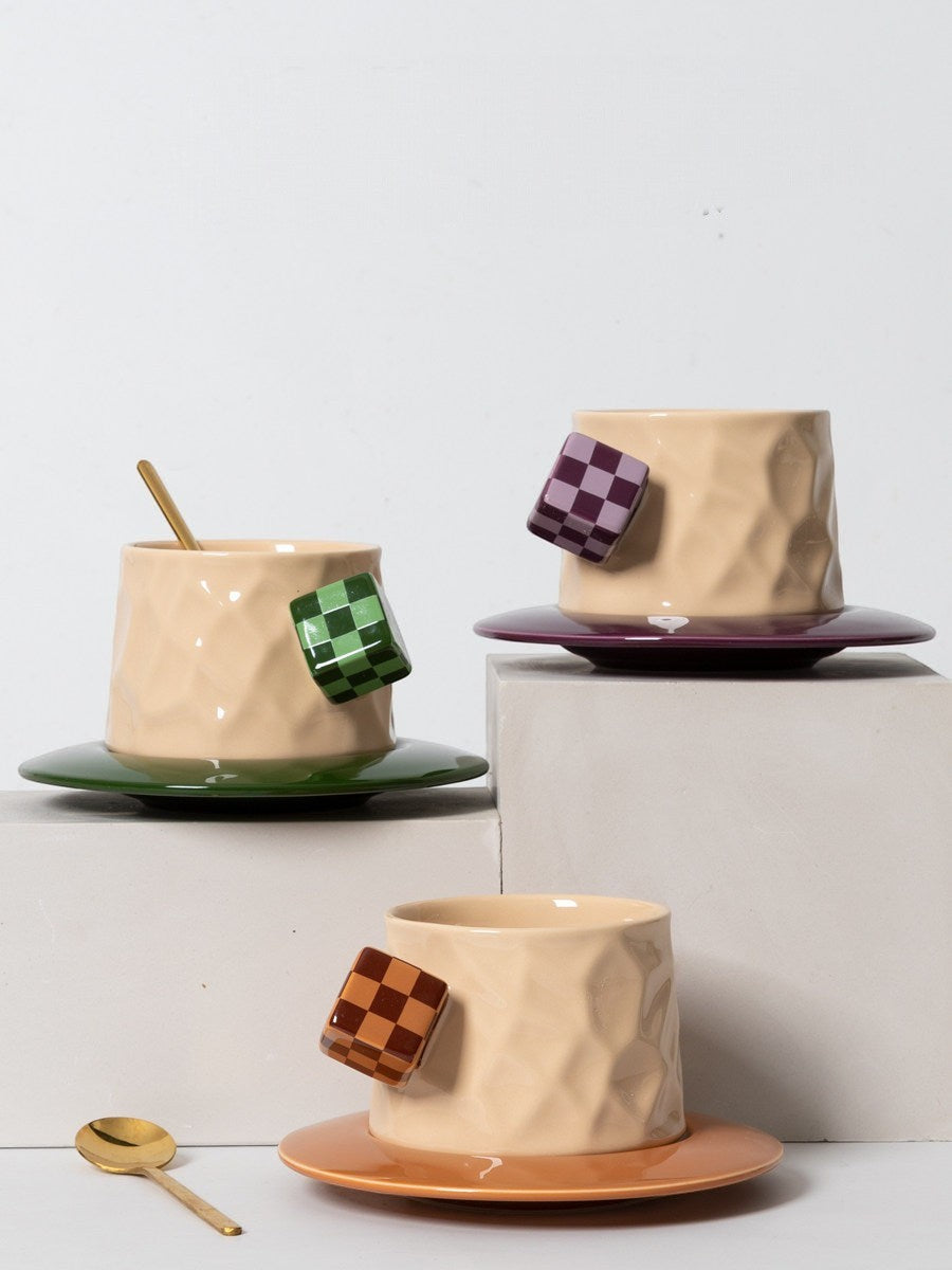HOMELIVY ceramic mugs with textured beige bodies, checkerboard cube handles, and matching saucers in green, purple, and orange.