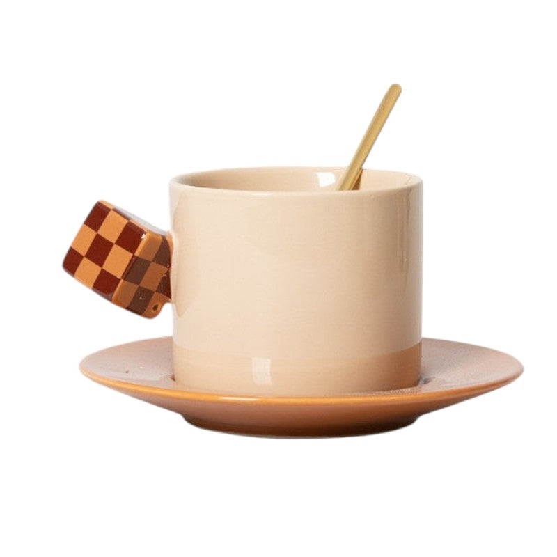 HOMELIVY beige ceramic coffee mug with a brown and tan checkerboard cube handle and matching saucer with gold spoon.