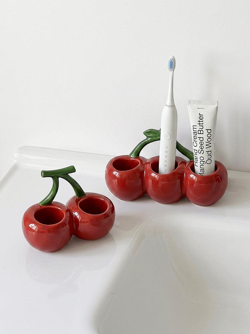 HOMELIVY cherry-shaped ceramic toothbrush holder in glossy red with green stems on a white bathroom sink