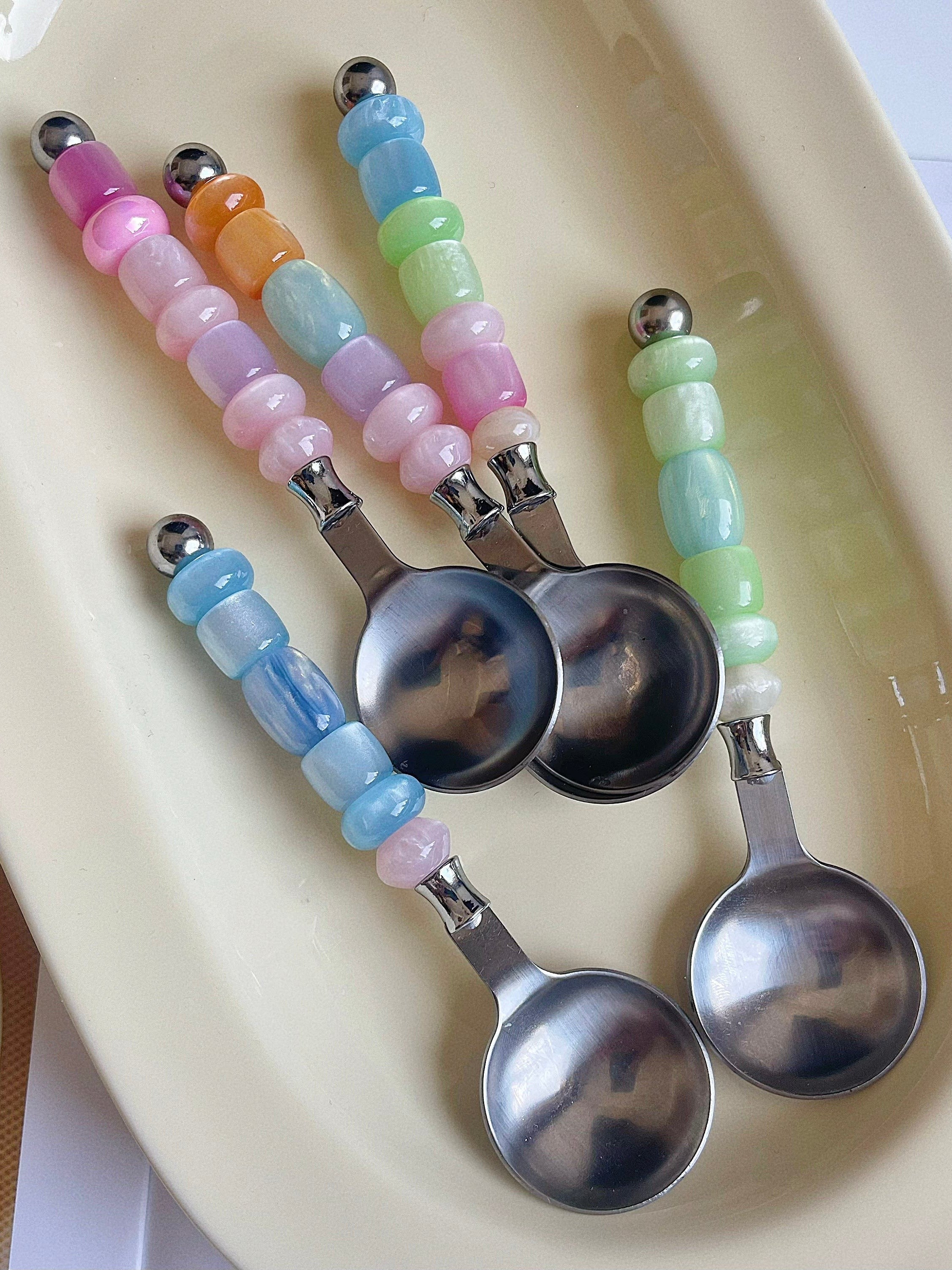 HOMELIVY colorful beaded spoons with stainless steel bowls and pastel resin bead handles on a cream tray.