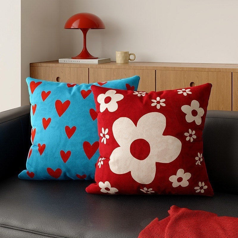 HOMELIVY decorative throw pillows featuring a red daisy flower pattern and a blue heart print on a black sofa.