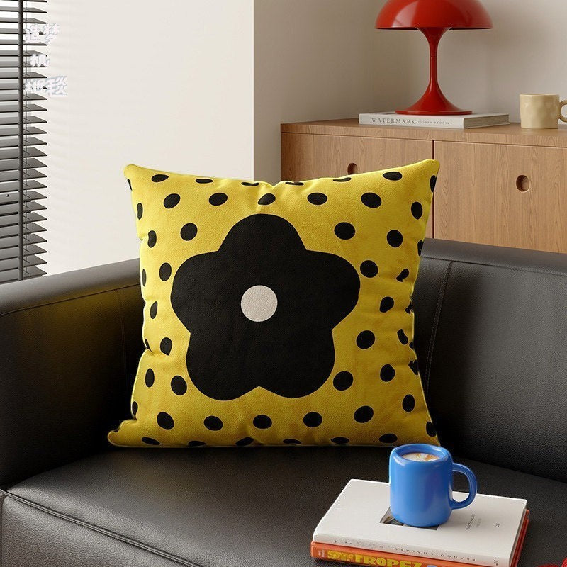 HOMELIVY yellow throw pillow with black polka dots and a large daisy flower design on a modern black sofa.