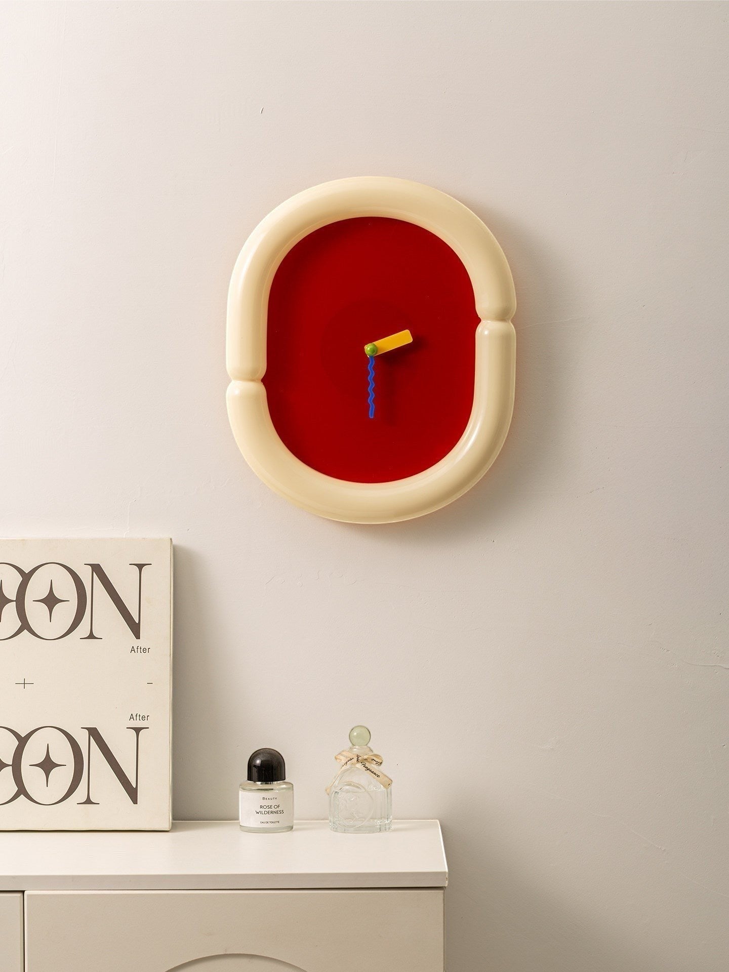 HOMELIVY funky wall clock with cream sculptural frame, red face, and multicolored hands. A bold, artistic timepiece.