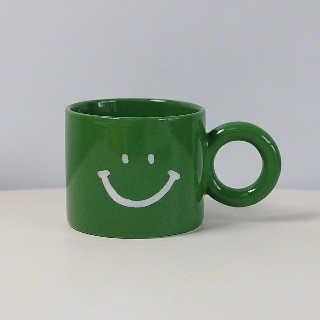 HOMELIVY green ceramic mug featuring a white smiley face print and a round circular handle on a white surface.
