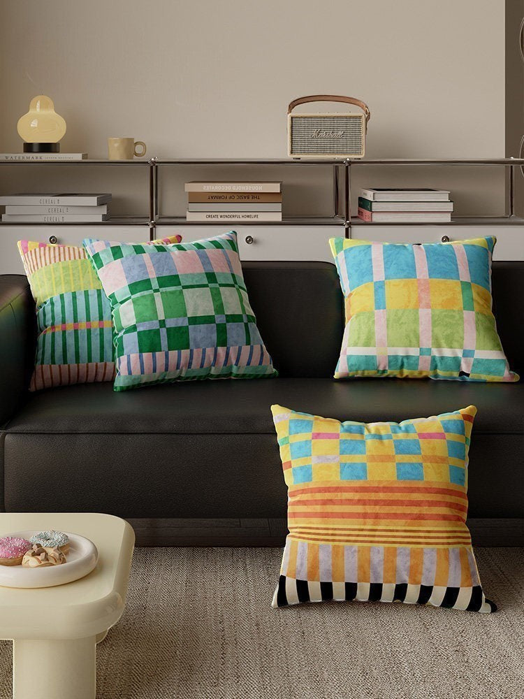 HOMELIVY maximalist throw pillows with vibrant check and stripe patterns in multi-colored velvet on a black sofa.