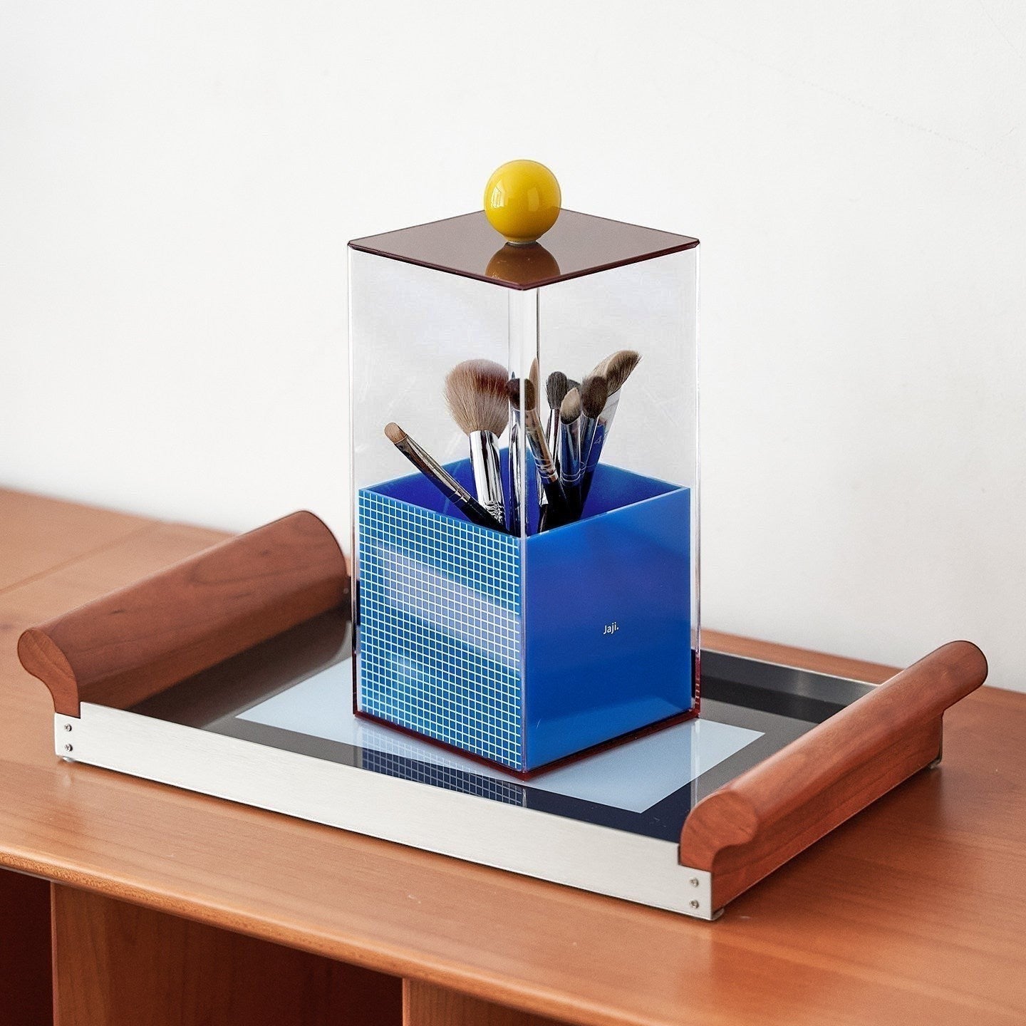 HOMELIVY Memphis acrylic brush holder with blue mosaic base and yellow knob on clear acrylic case, holding makeup brushes.