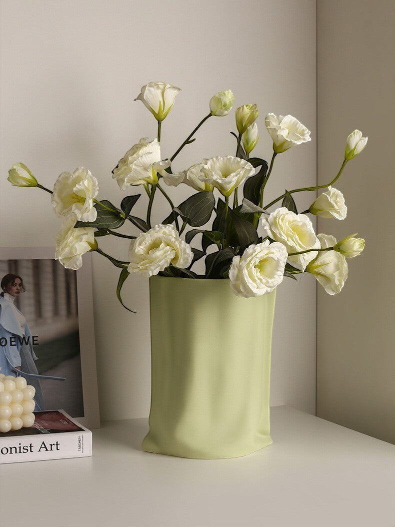HOMELIVY light green ceramic paper bag vase with a modern crinkled texture holding a bouquet of white flowers.