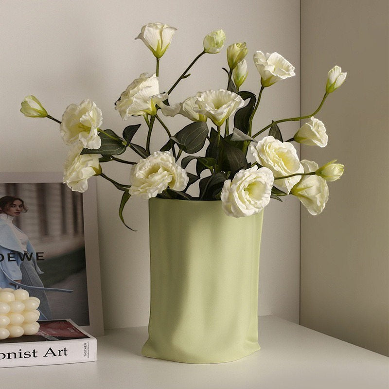 HOMELIVY light green ceramic vase with a unique crinkled paper bag design holding a bouquet of white flowers.