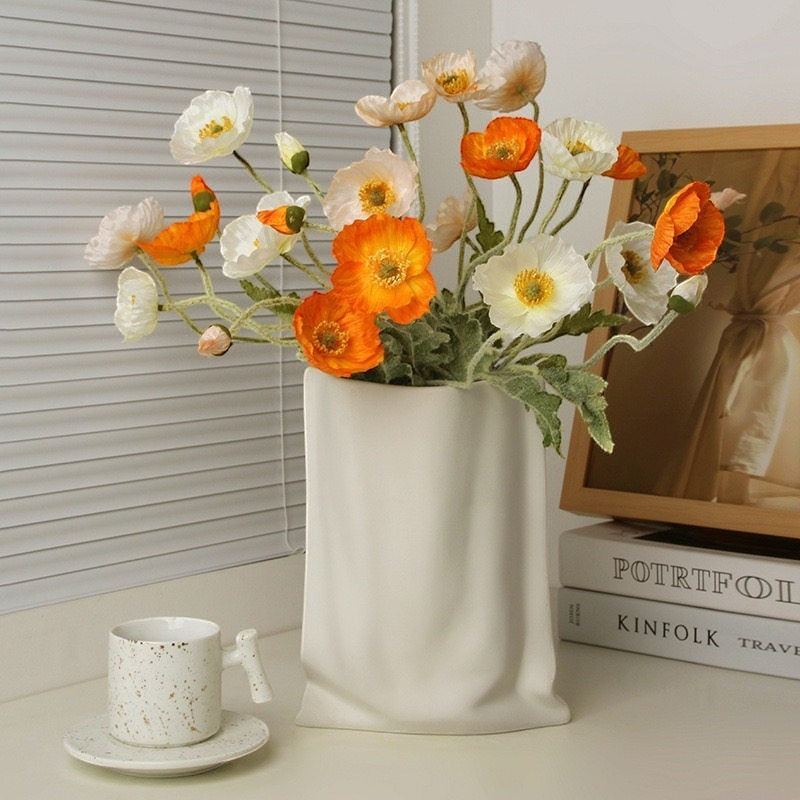 HOMELIVY white ceramic paper bag vase holding a bouquet of vibrant orange and white artificial poppy flowers.