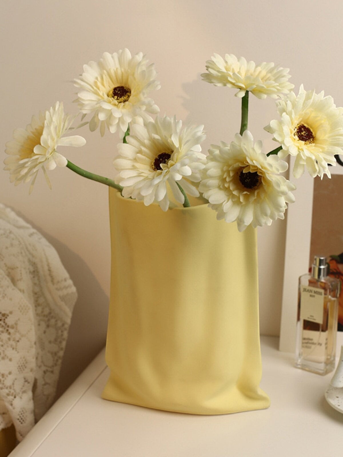 HOMELIVY yellow ceramic vase shaped like a paper bag, holding a bouquet of cream-colored artificial flowers.