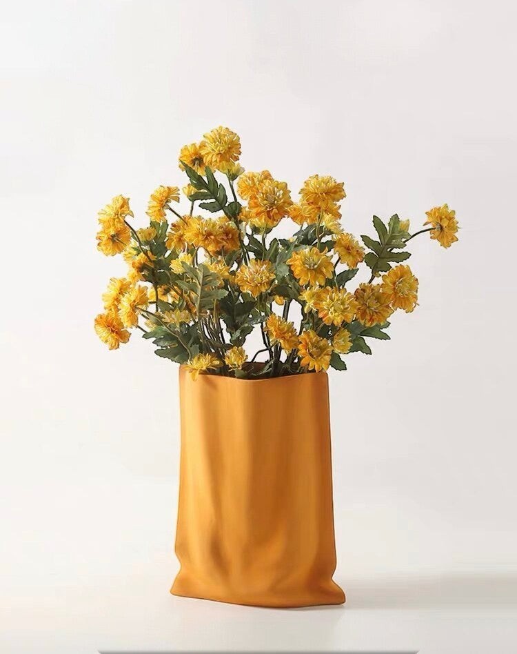 HOMELIVY yellow ceramic paper bag vase filled with a bouquet of vibrant yellow artificial chrysanthemums.