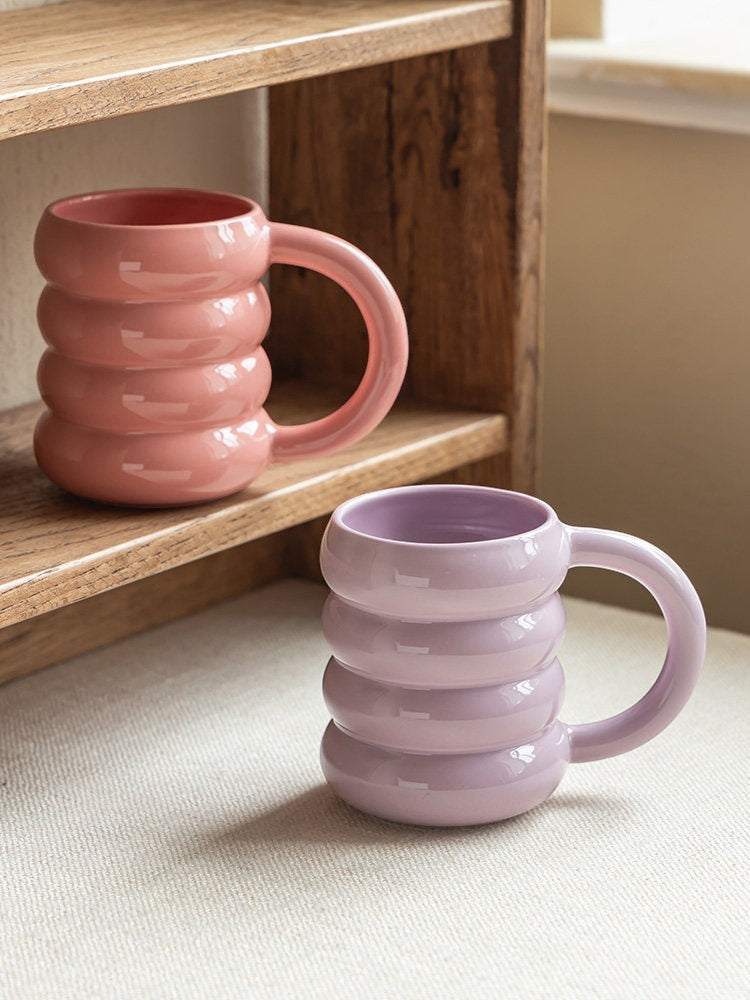 HOMELIVY pastel doughnut mugs in pink and lavender ceramic with a ribbed, rounded design on a wooden shelf.