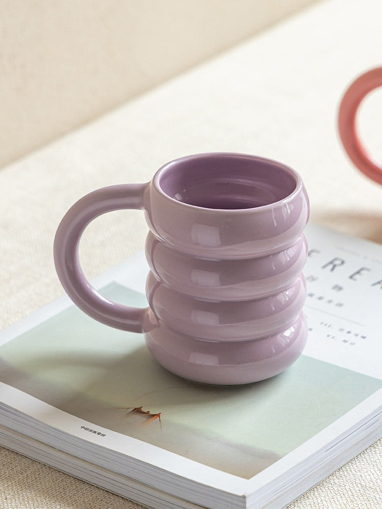 HOMELIVY pastel purple ceramic doughnut mug with a unique ribbed, stacked ring design sitting on a magazine.