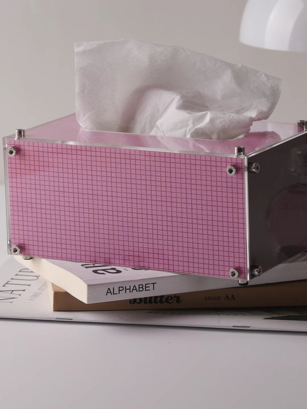 HOMELIVY pink acrylic tissue box with a modern grid pattern, resting on a stack of books.
