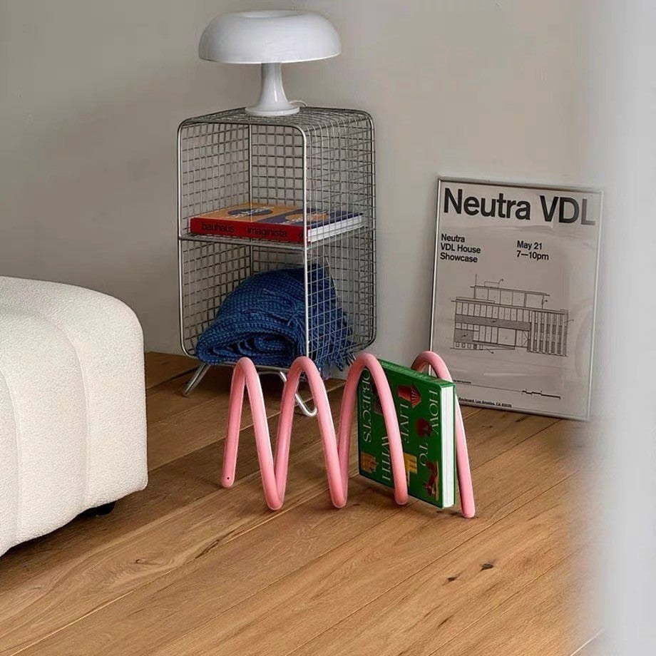 HOMELIVY pink spiral book holder with a wave design, holding a book on a wooden floor in a modern living room.