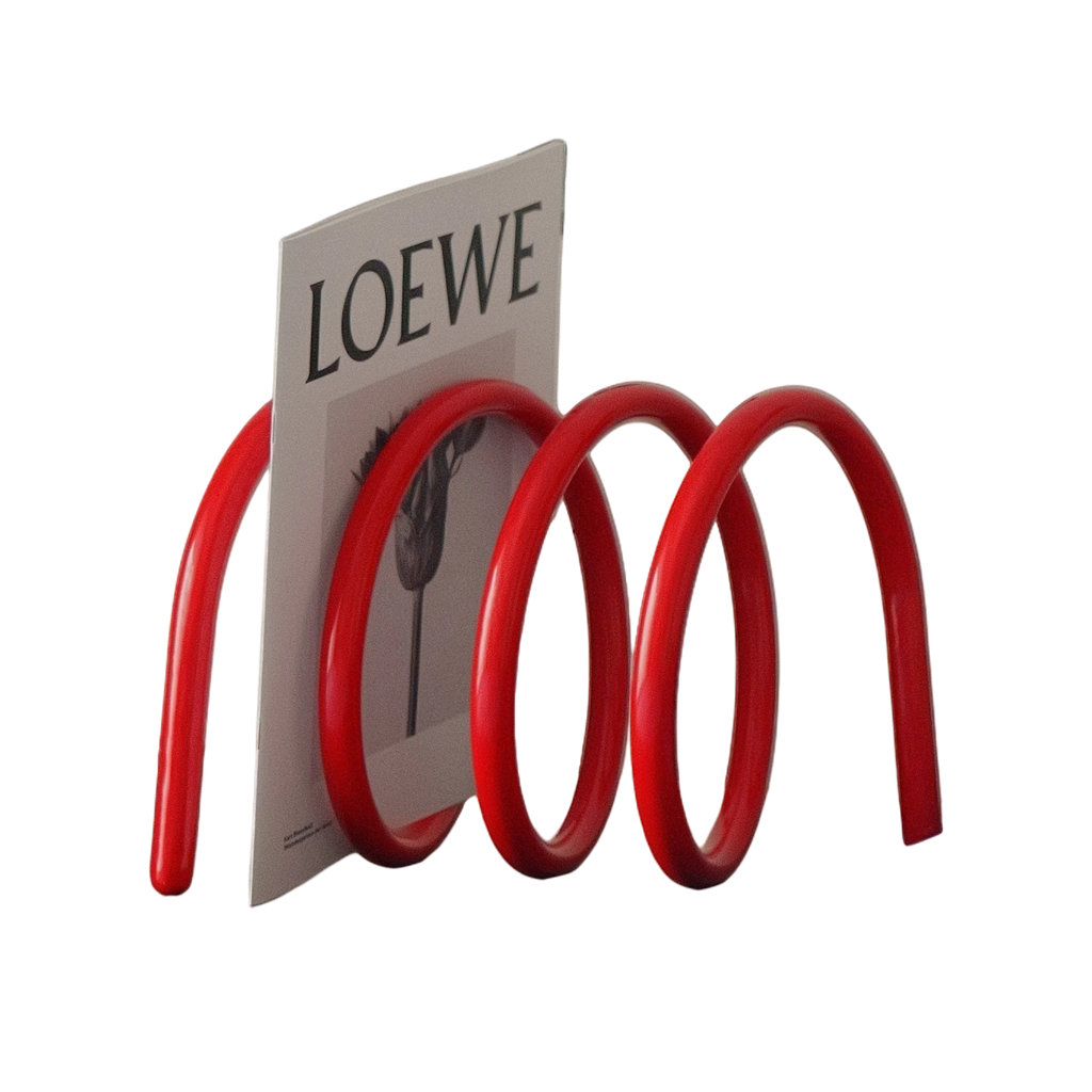 HOMELIVY red spiral book holder with a sculptural wave design, displayed on a modern cabinet with a magazine.