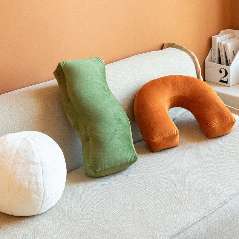 HOMELIVY sculptural velvet cushions: burnt orange arch, green bolster, and white sphere on a sofa.