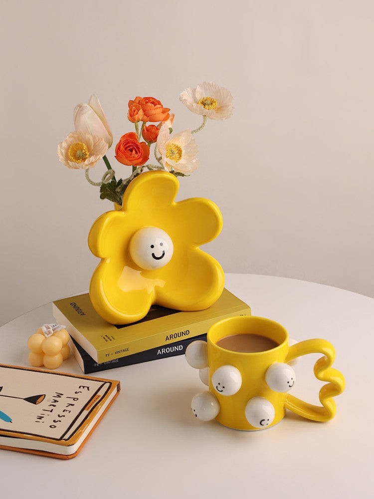 HOMELIVY yellow ceramic flower-shaped vase with a smiley face center, holding orange and white artificial flowers.