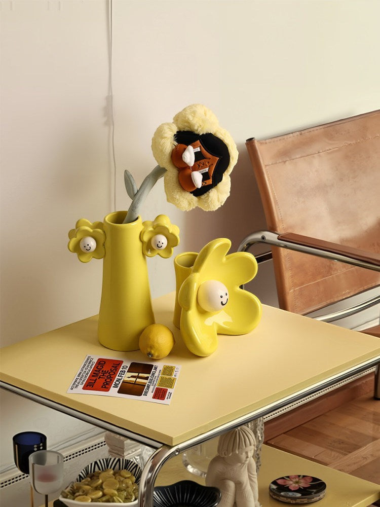 HOMELIVY yellow ceramic smiley flower vases on a yellow table with a plush flower and lemon decor.